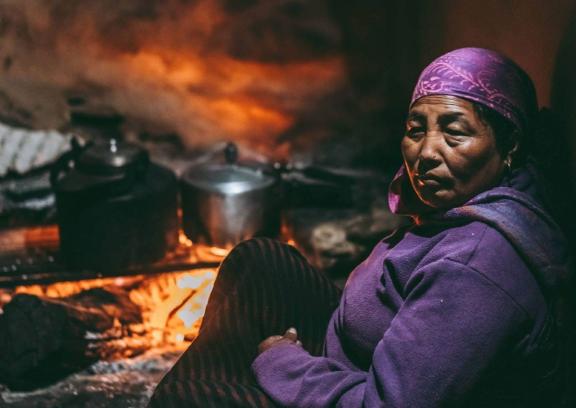 An elderly woman sitting by a traditional cookstove. Source: Vladimir Soic/Shutterstock.com